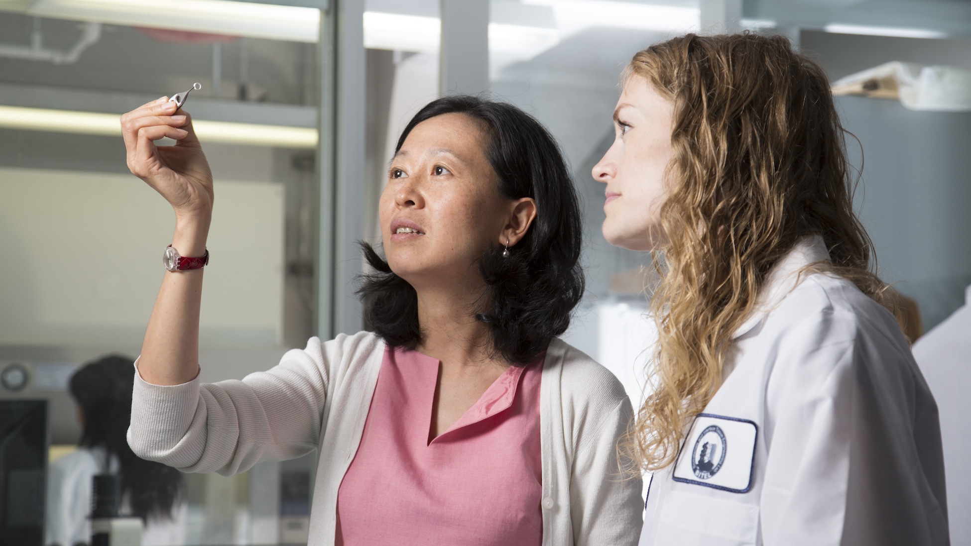 A Biomedical Engineering student in a white lab coat and professor inspecting a biomedical sample