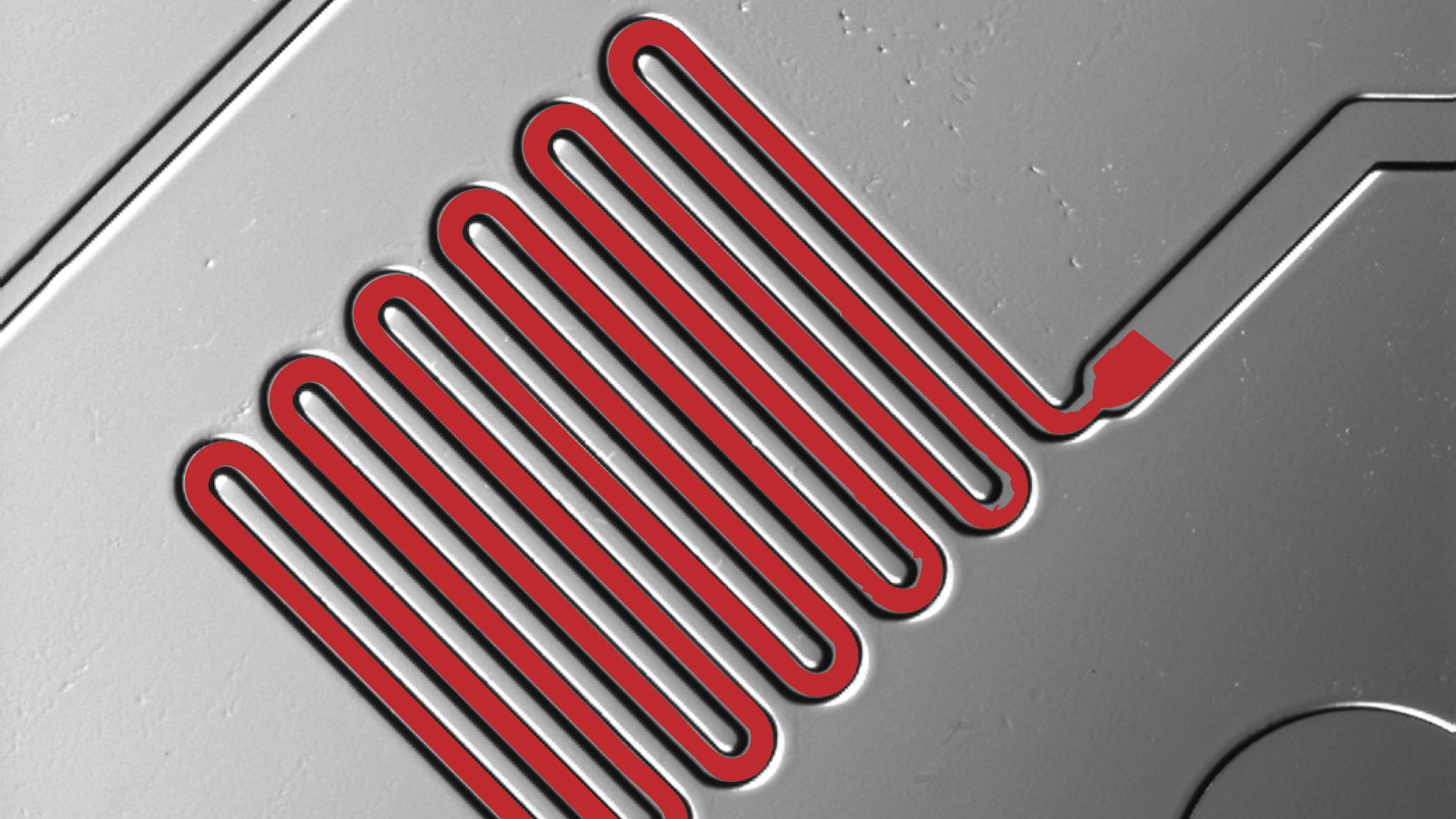 Close-up of a microfluidic chip showing a red serpentine channel pattern etched into a gray surface.