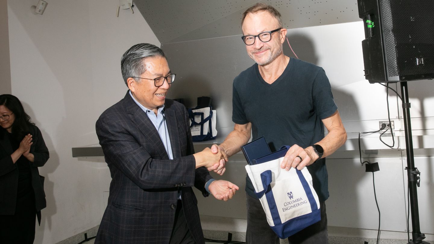 Harry West shakes hands with Dean Shih-Fu Chang while holding a Columbia Engineering tote bag.