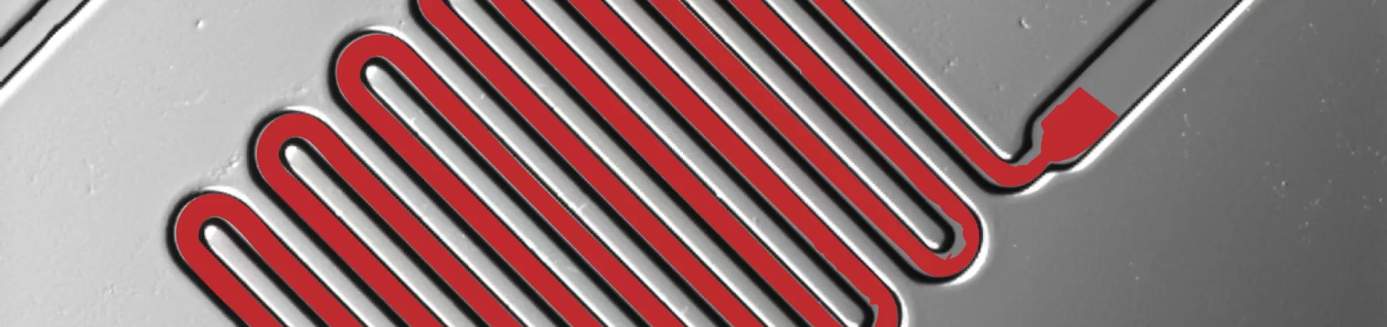 Close-up of a microfluidic chip showing a red serpentine channel pattern etched into a gray surface.